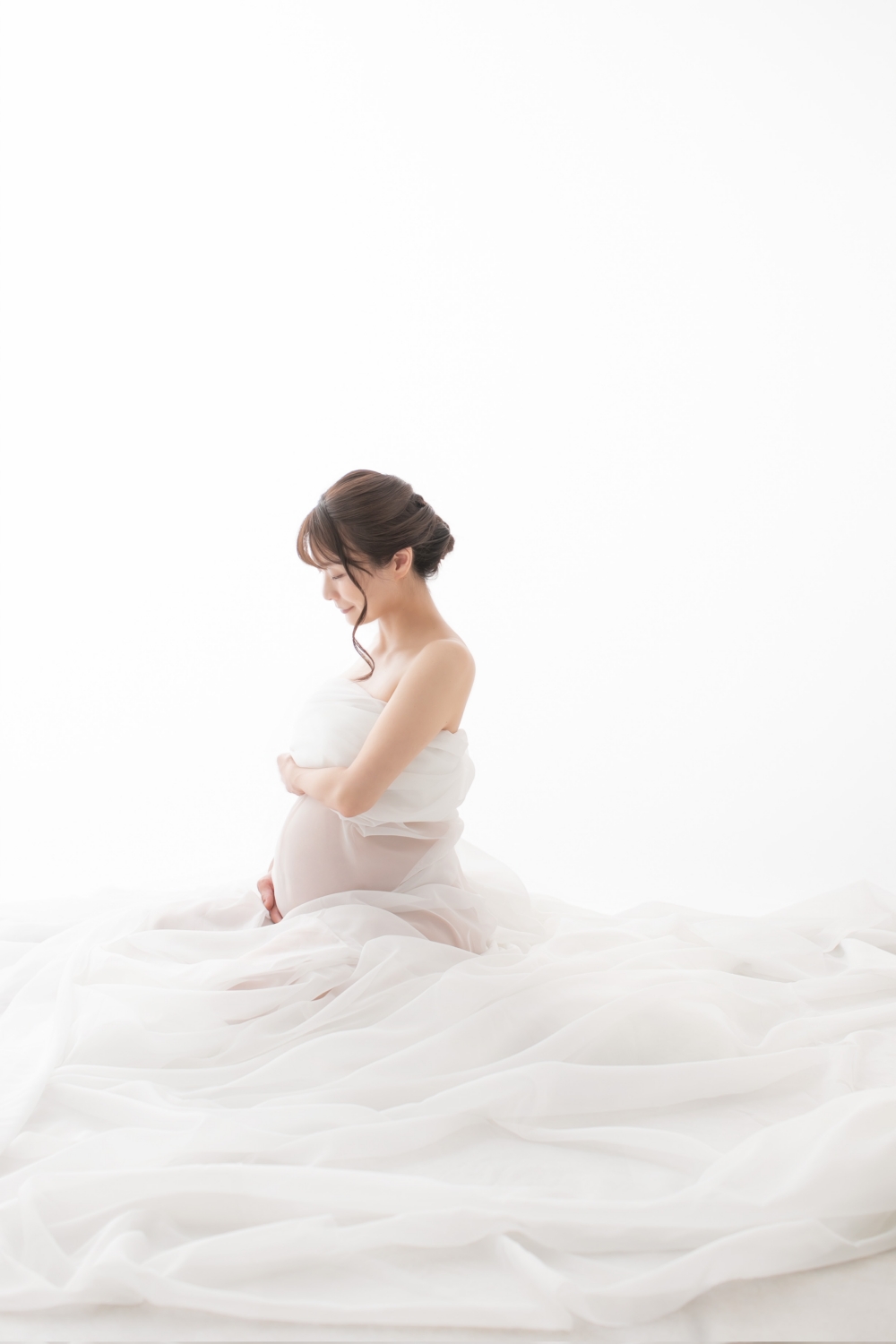 白いチュールに包まれ、お腹に手を当てて座っている妊婦さんの写真