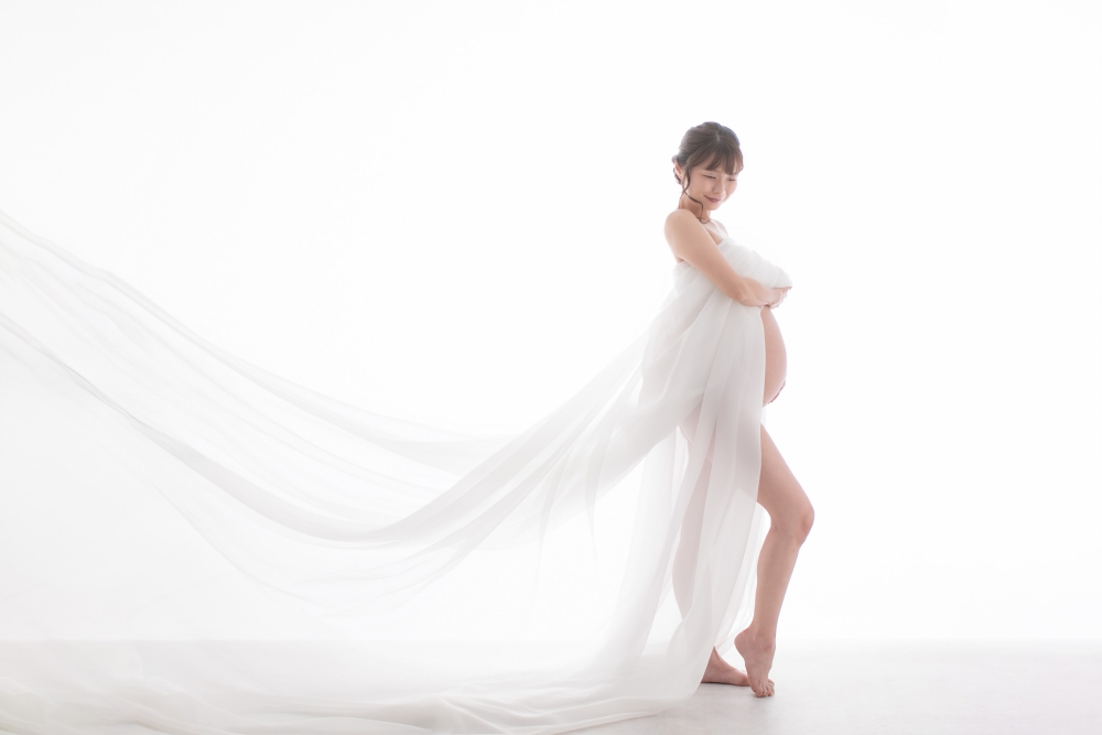 白いチュールをなびかせ、凛と立つ妊婦さんの写真